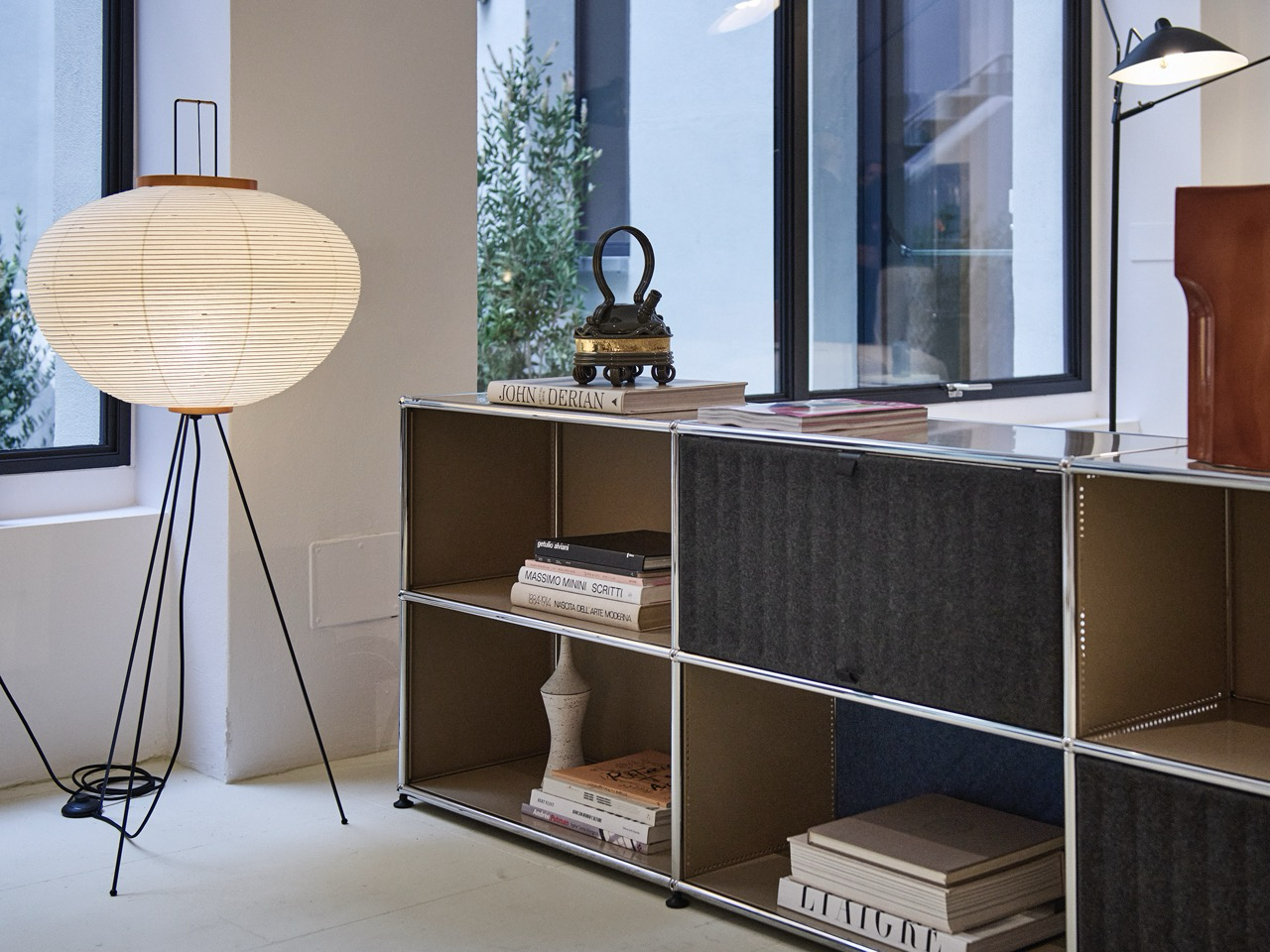 Low USM Haller sideboard with open compartments and felt fronts, holding art books and ceramics; a paper lantern floor lamp beside it.