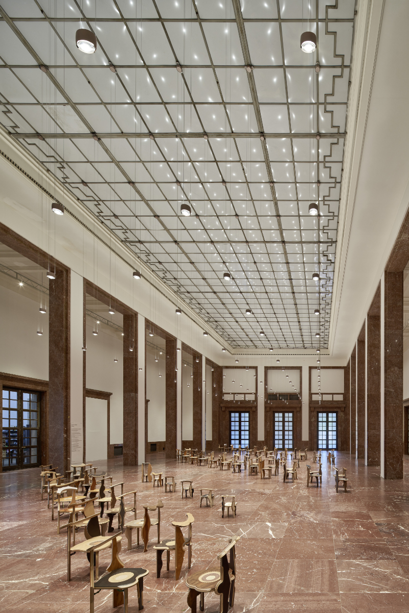 Mittelhalle im Haus der Kunst München mit Stühlen der Installation „Sitzung“ von Martino Gamper und zahlreichen Pendelleuchten von Occhio an der Decke.