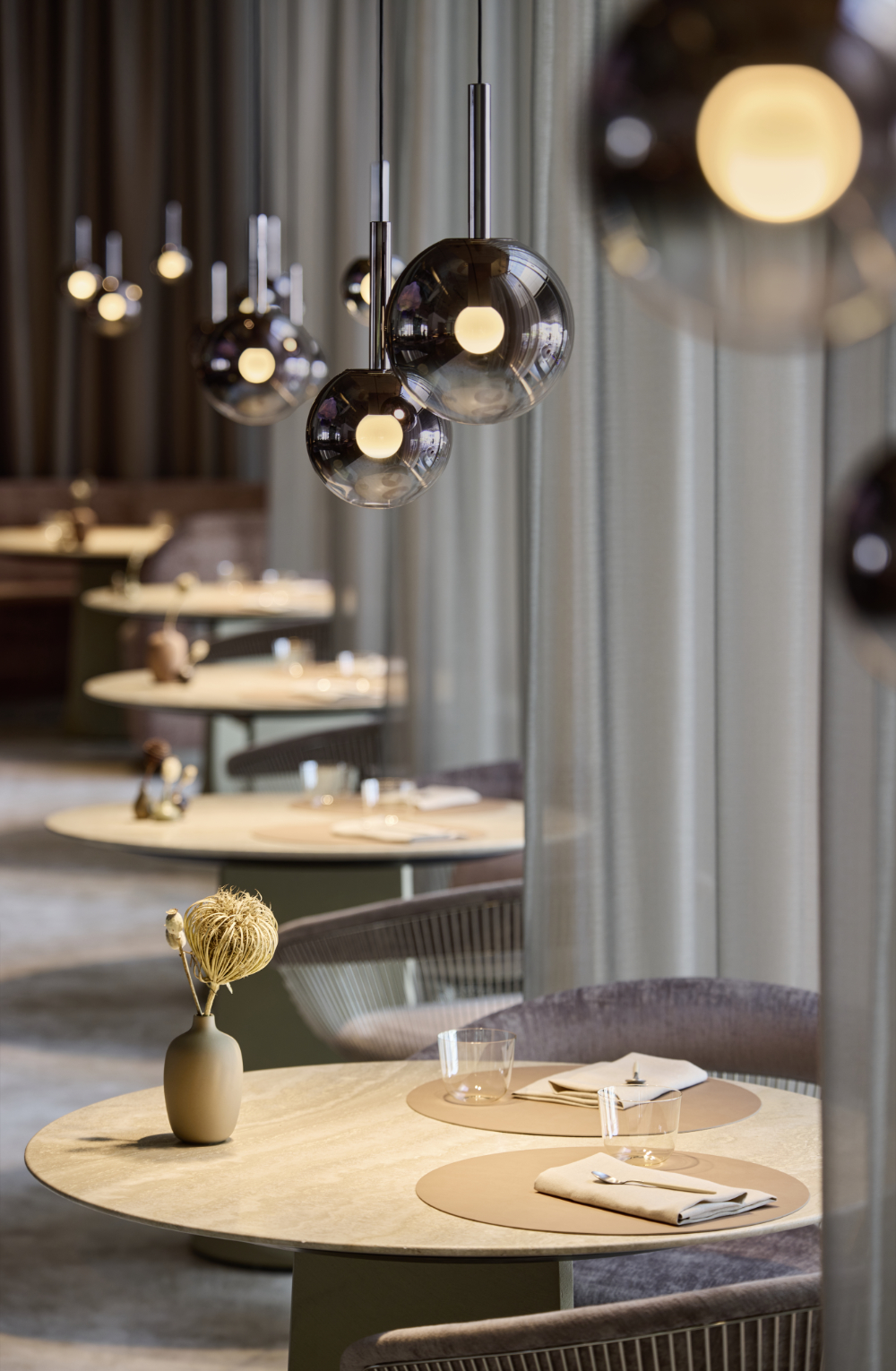 Restaurantbereich von The Cloud by Käfer in der BMW Welt München mit runden Tischen, Vorhängen und mehreren kugelförmigen Pendelleuchten von Occhio.