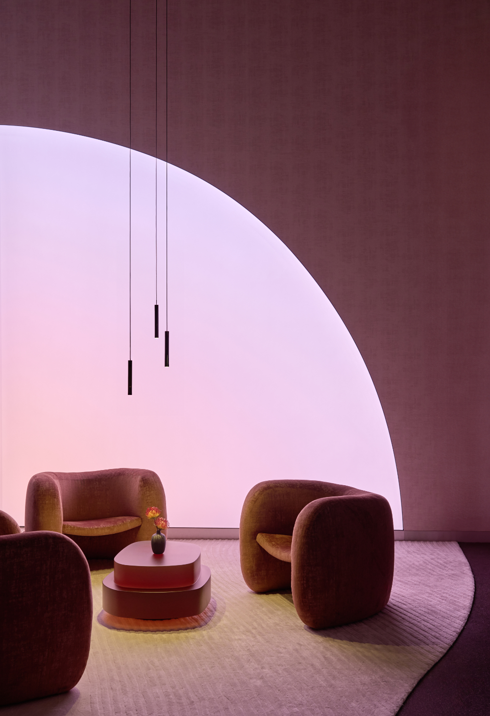 Loungebereich von The Cloud by Käfer in der BMW Welt München mit rosafarbenem Raumlicht, Sesseln, rundem Tisch und schlanken Pendelleuchten von Occhio.
