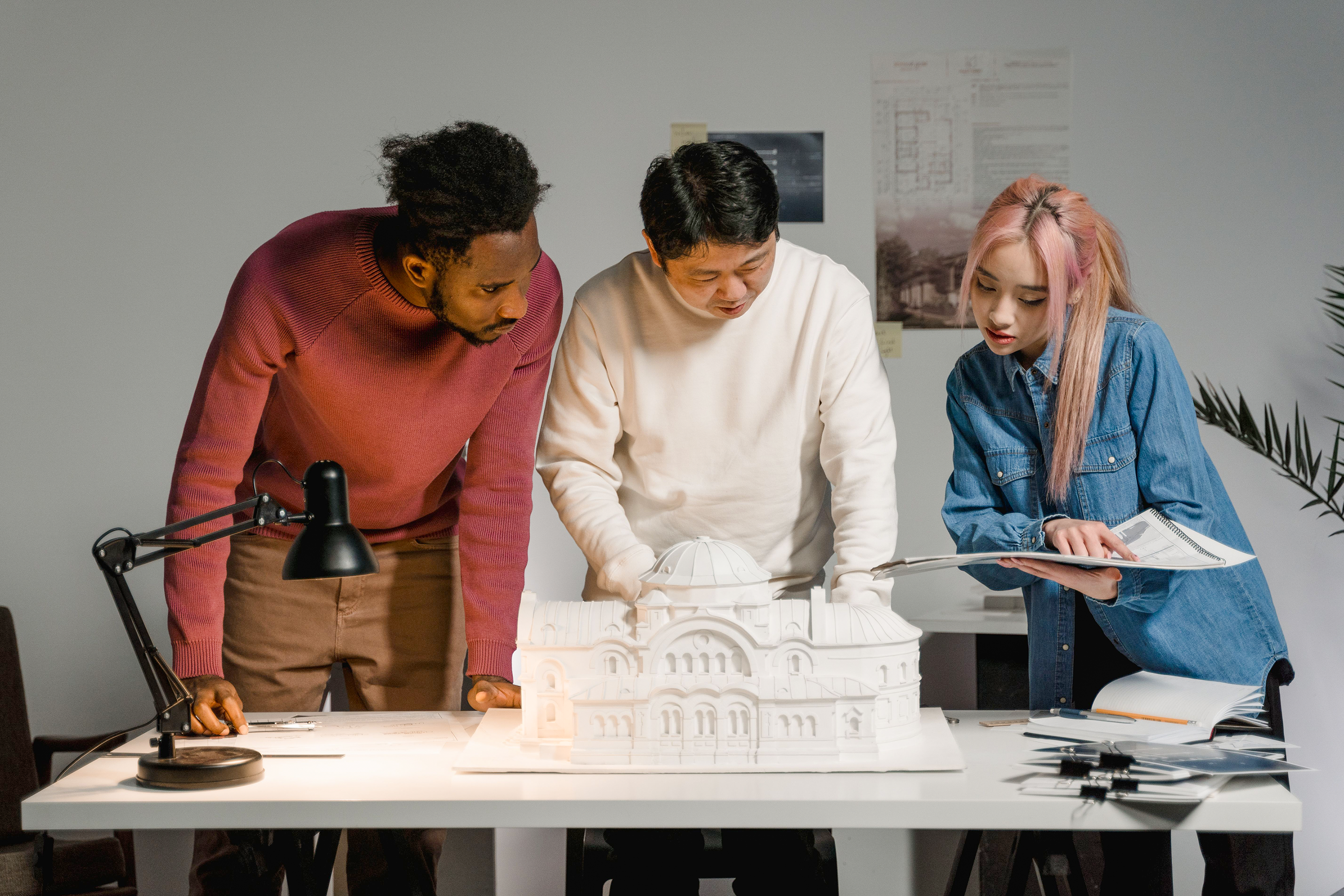Three designers discussing an architectural model and documents at a table.