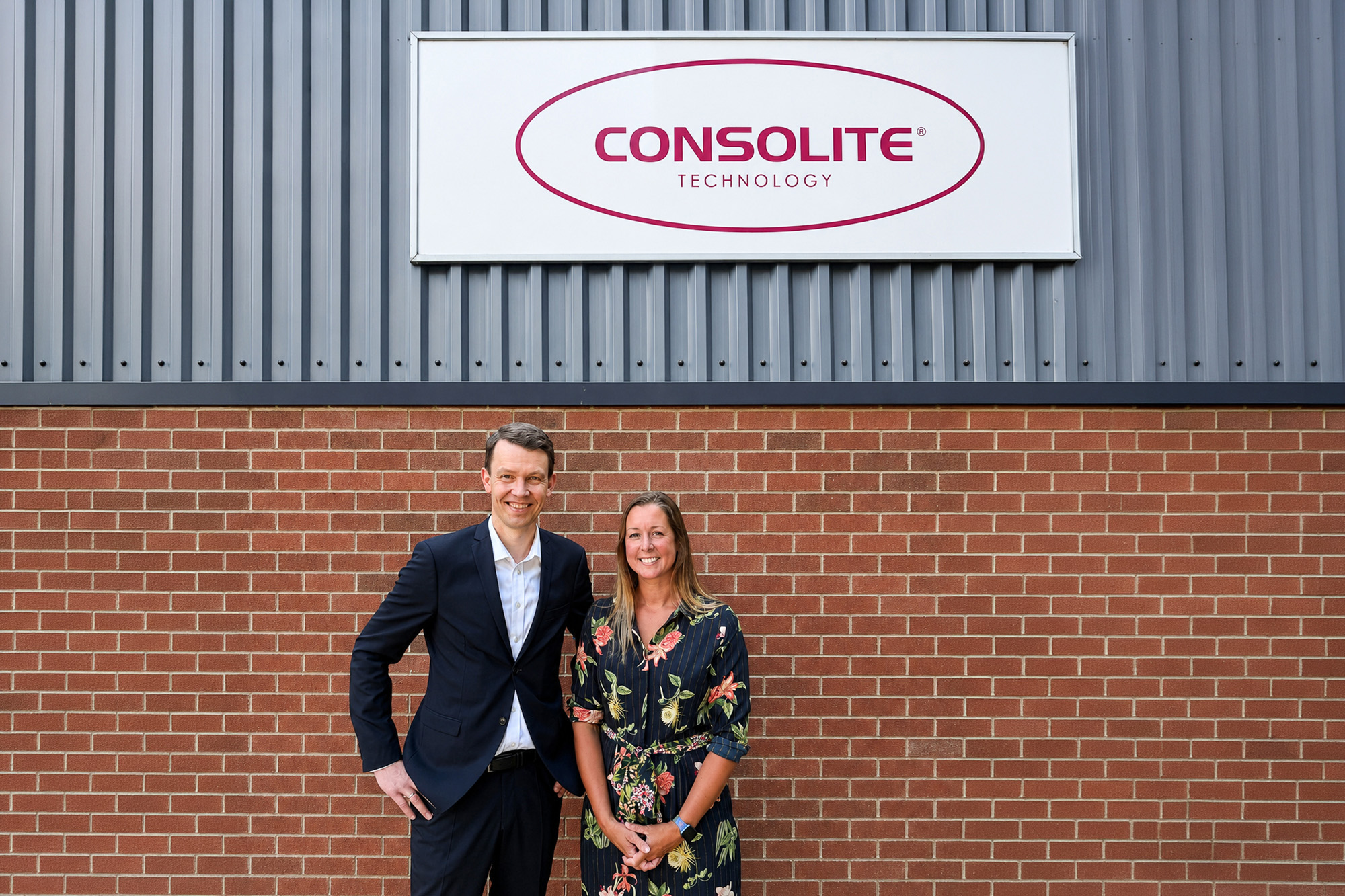 Tommy Stranden of Glamox and Lyndsey Eriksson of Consolite standing outside the Consolite building beneath the company sign.
