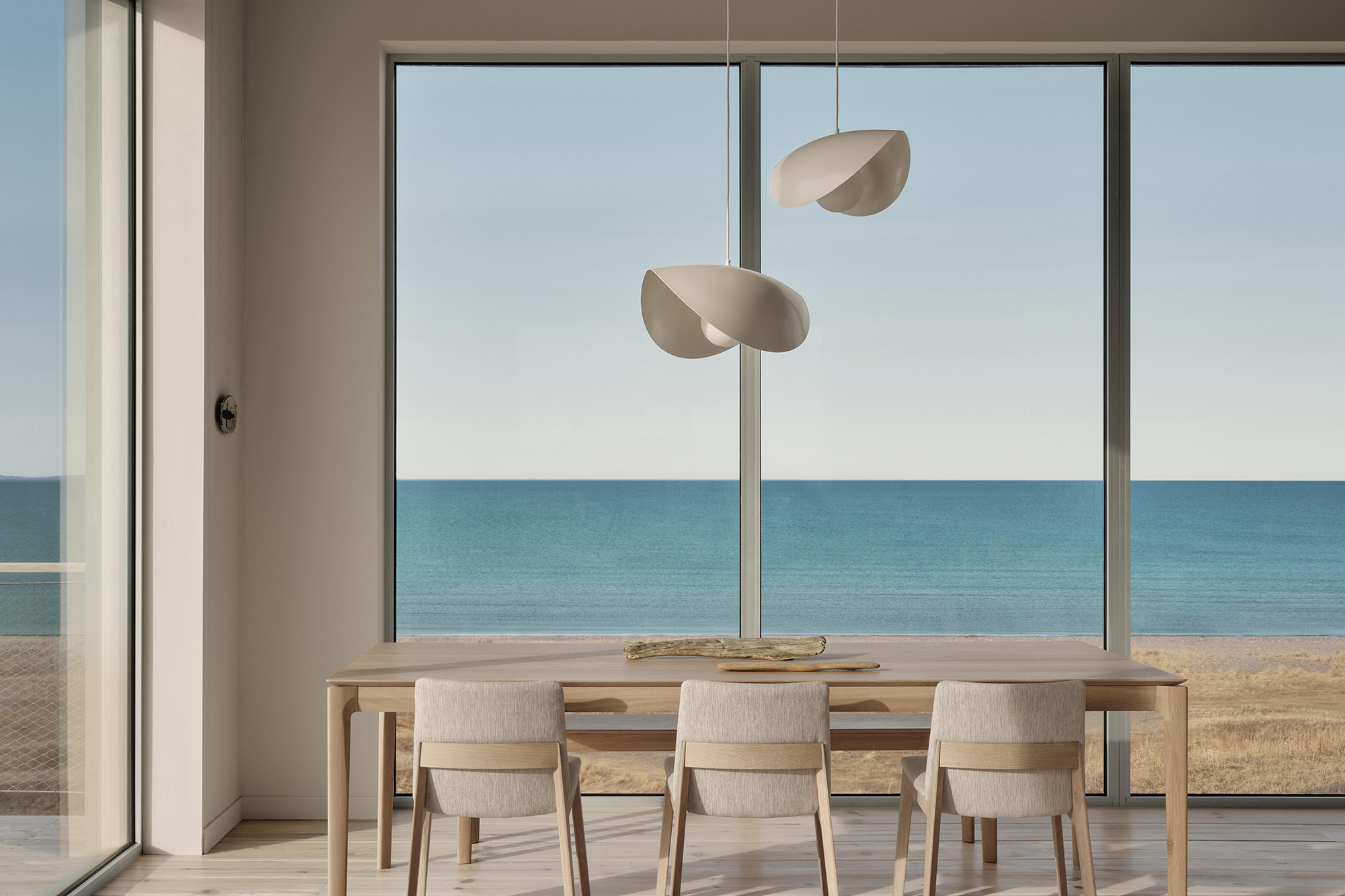 Large windows frame the Atlantic like a quiet landscape painting. The dining area, furnished by Ethnicraft and lit by Luminaire Authentik, faces directly towards the sea.