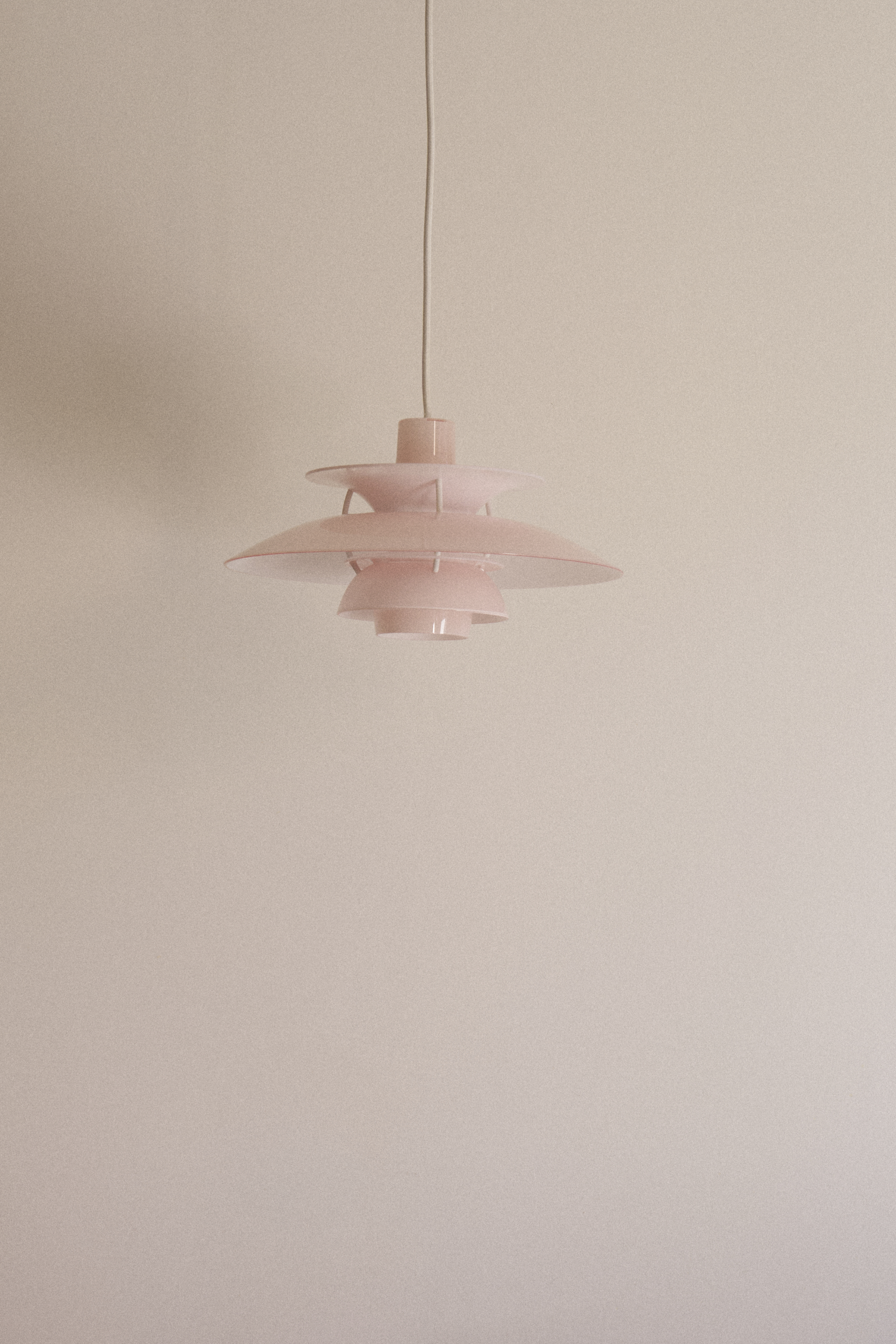 Rosafarbene Pendelleuchte PH 5 von Louis Poulsen vor heller Wand.