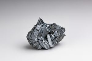 Silver-grey metallic antimony crystal on a light background.