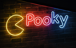 Neon sign spelling “Pooky” in red, pink and blue next to a yellow Pac-Man symbol on a dark brick wall.