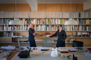 Kim Colin and Sam Hecht stand in their London studio Industrial Facility in front of bookshelves and worktables.