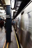 Bahnsteig der New Yorker U-Bahn-Station „Wall Street"; rechts rauscht ein einfahrender Zug in Bewegungsunschärfe vorbei, während Fahrgäste warten.