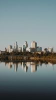 Skyline von Minneapolis mit Hochhäusern, Bäumen und Spiegelung im Mississippi bei klarem Himmel.
