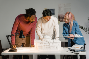 Three designers discussing an architectural model and documents at a table.
